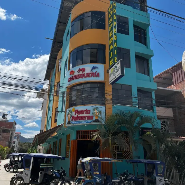 Fachada de Puerto Palmeras: edificio turquesa con letreros de marisquería, hospedaje y garaje